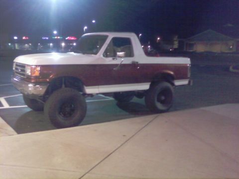 1989 Ford Bronco - A two-tone white and maroon Ford Bronco is parked outside at night.
