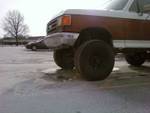 1989 Ford Bronco - A lifted 1987-1991 Ford F-Series truck sits in a snowy lot, showing its front corner and wood paneling.