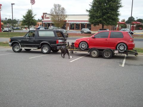 1989 Ford Bronco - A black 1989 Ford Bronco is parked in a lot, towing a red Volkswagen Golf on a trailer.