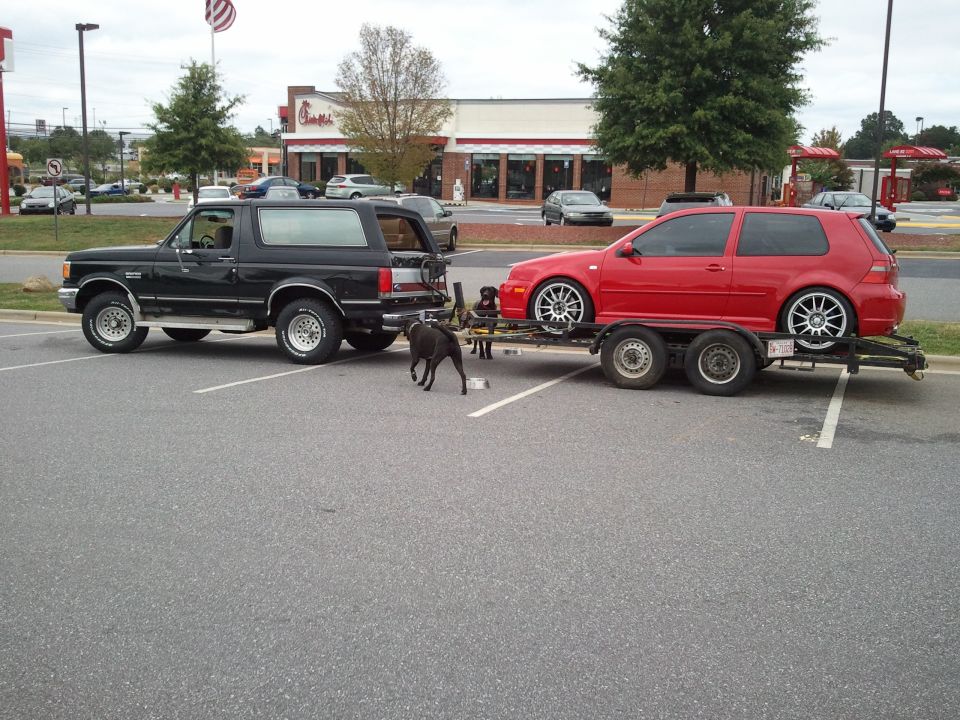 Black 1989 Ford Bronco side view, towing a red Volkswagen Golf
