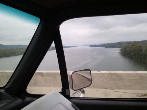1989 Ford Bronco - View from inside a vehicle traveling over a bridge, with a river and forested landscape visible.