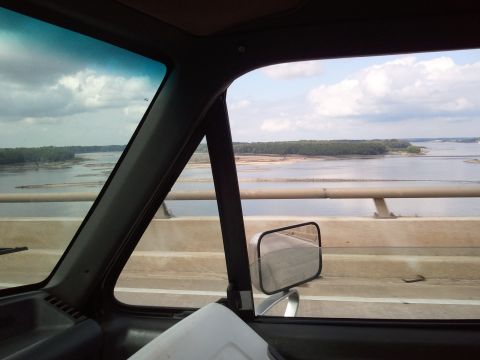 1989 Ford Bronco - View from inside a vehicle crossing a bridge over a wide river on a cloudy day.