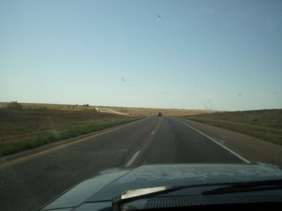 Car hood on highway with distant vehicle under clear sky