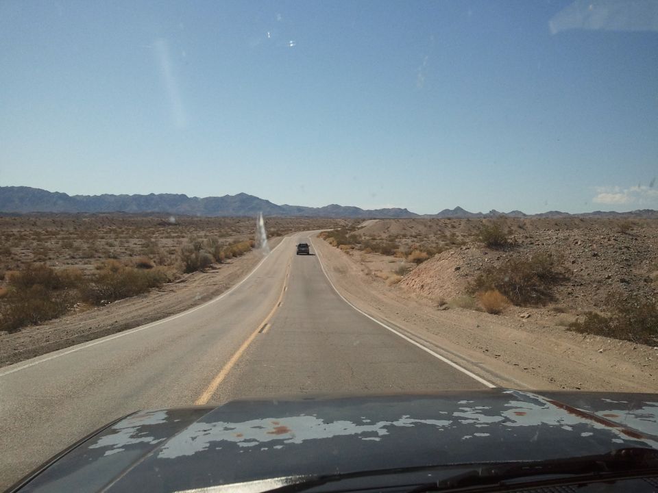 Desert highway with a distant vehicle under a clear blue sky