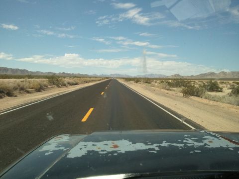 1989 Ford Bronco - A long, empty highway stretches through a desert landscape under a partly cloudy sky.
