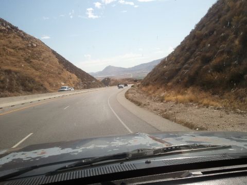 1989 Ford Bronco - View from inside a vehicle driving on a highway through a mountainous landscape with other cars visible ahead.