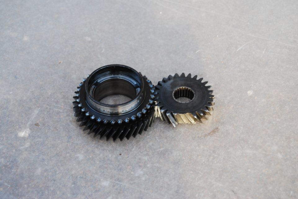 Two helical transmission gears, one large black with collar, one small splined, on concrete.