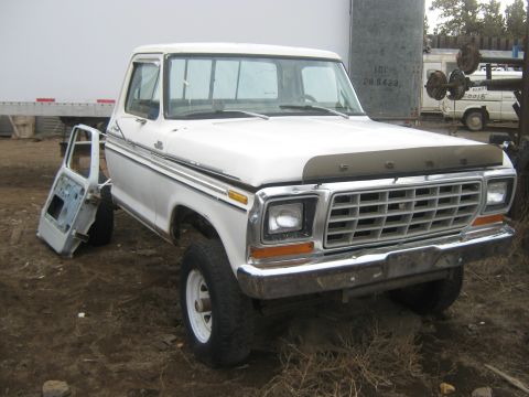 1978 Ford Bronco - A white Ford F-Series truck, missing its driver's side door, sits in an outdoor lot.