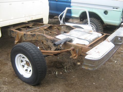 1978 Ford Bronco - The chassis and fuel tank of a disassembled truck are shown, with another vehicle in the background.