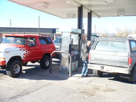 1979 Ford Bronco - A red and white Ford Bronco with flame decals is at a gas station next to another SUV.