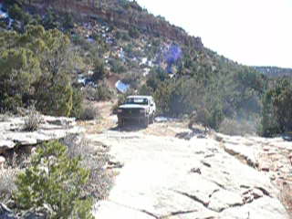 1979 Ford Bronco - A white SUV navigates a rough dirt road through a dry, mountainous terrain.