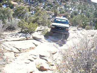 1979 Ford Bronco - A white SUV navigates a challenging rocky path in a desert landscape, with a Super Motors logo in the lower right corner.