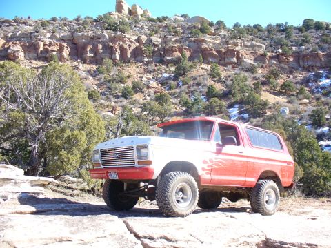 1979 Ford Bronco - A red and white Ford Bronco with flame decals sits on a rocky surface with a mountainous backdrop.