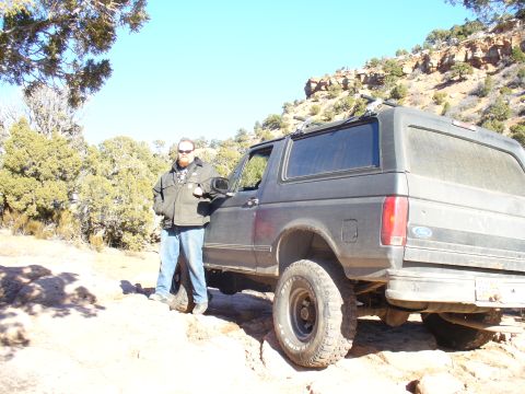 1979 Ford Bronco - Man poses with a dark Ford Bronco on a dirt trail with rocky hills in the background.