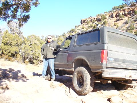 1979 Ford Bronco - A man stands next to a Ford Bronco on a , off-road trail under a clear blue sky.