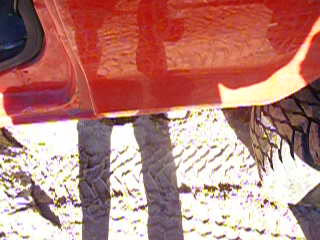 1979 Ford Bronco - Close-up of a red vehicle's side panel, showing reflections and a portion of the tire.