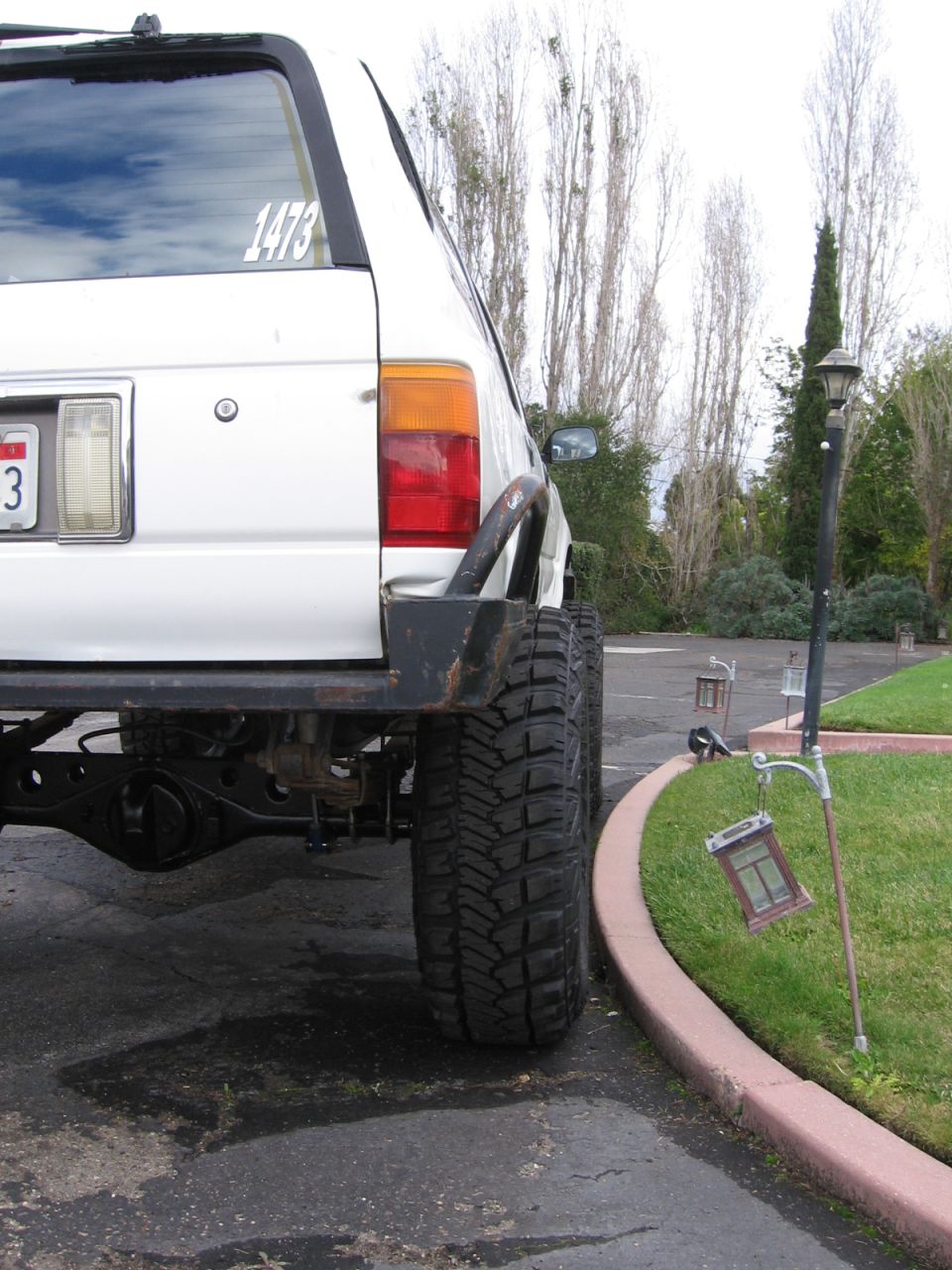 White SUV rear axle, aftermarket bumper, and large tire. Number 1473 sticker on rear window