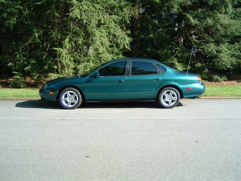1997 Ford Taurus - Side profile of a green 1997 Ford Taurus sedan parked on the side of a road.