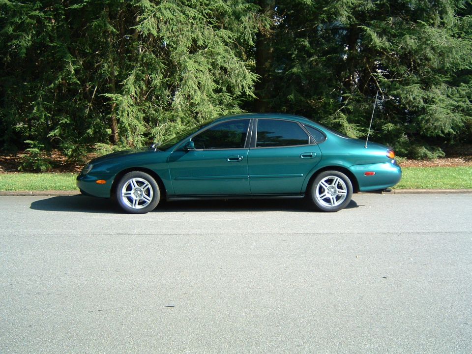 1997 Ford Taurus sedan, side view, green paint, parked on asphalt next to trees