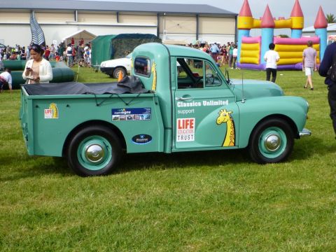 1969 MINI Cooper - A vintage green pickup truck is parked on grass at an outdoor event with a bouncy castle in the background.