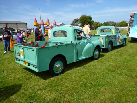 1969 MINI Cooper - Two vintage green pickup trucks are parked on a grassy field, with one towing the other.