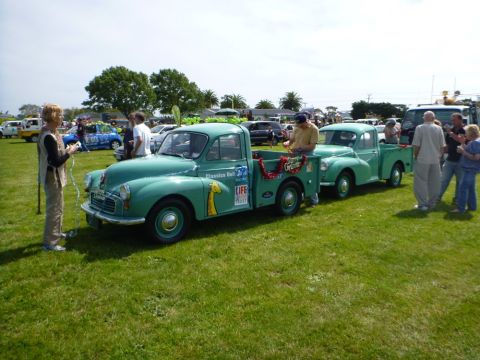 1969 MINI Cooper - A green pickup truck tows a trailer carrying a matching car, with "Classics Bull" visible on the truck's door.