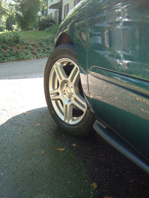1997 Ford Taurus - The side of a green sedan is shown, focusing on the front wheel and tire.
