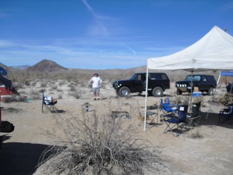 1986 Ford Bronco - Two black Ford Broncos are parked at a desert campsite under a clear blue sky.