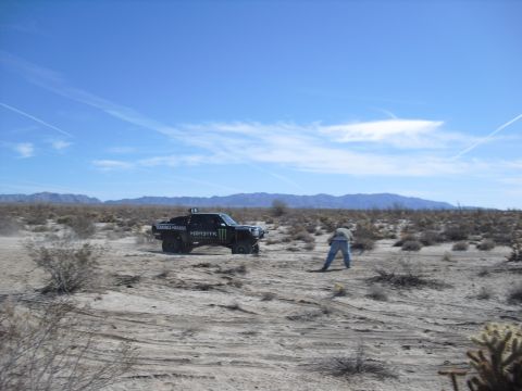 1986 Ford Bronco - A desert scene with a modified truck and a person in the dry, scrubby terrain under a bright blue sky.