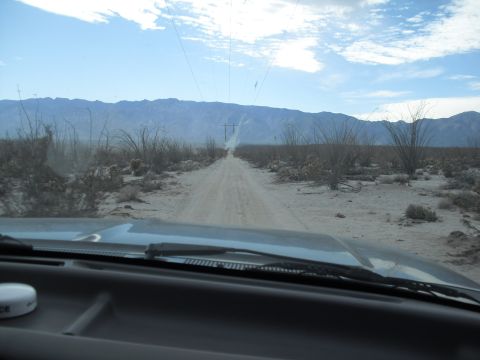 1986 Ford Bronco - View from inside a vehicle driving on a dusty desert road towards distant mountains.