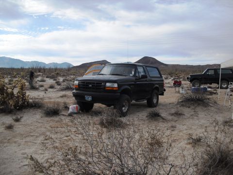 1986 Ford Bronco - Two black Ford Broncos are parked in a desert setting under a cloudy sky.