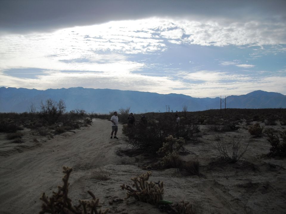 Desert landscape with mountains in background, dirt road, and three people standing