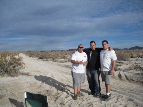 1986 Ford Bronco - Three men pose for a photo on a dusty desert road, with scrub brush and distant mountains in the background.