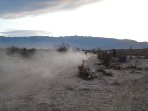 1986 Ford Bronco - A vehicle races through a dusty desert landscape with spectators watching.