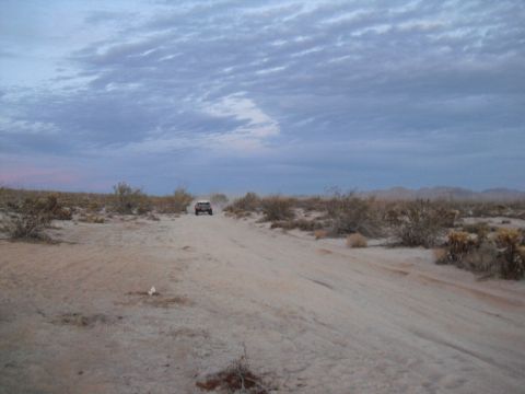 1986 Ford Bronco - A lone SUV navigates a dusty track through a barren desert environment.