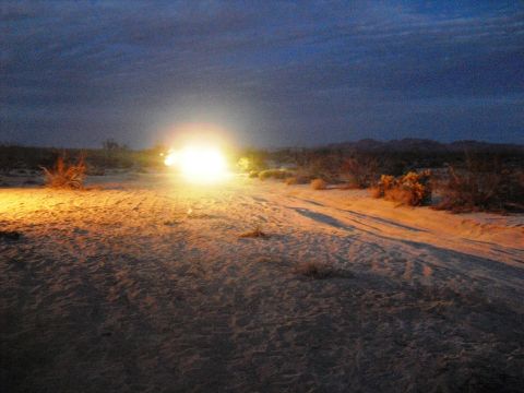 1986 Ford Bronco - A vehicle navigates a dusty desert track at twilight, its headlights cutting through the dim light.