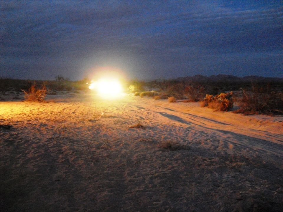 Off-road vehicle with bright headlights on a desert dirt road at dusk