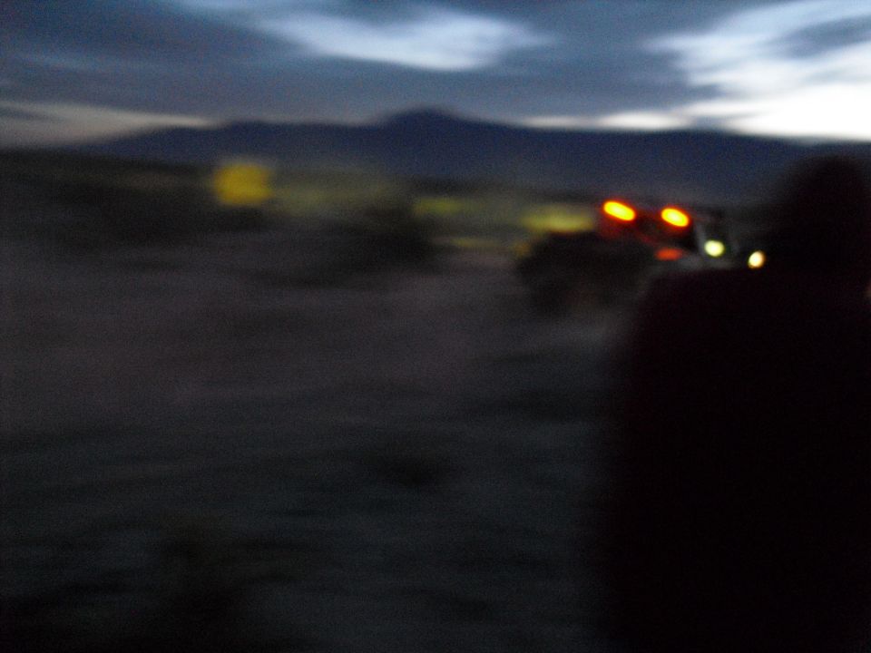 Several off-road vehicles with lights on in a desert landscape at dusk