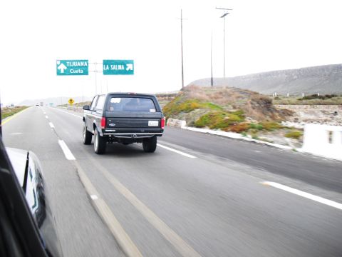1986 Ford Bronco - Black Ford Bronco driving on a highway with directional signs in the background.