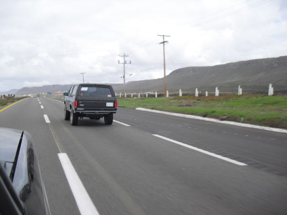 Black SUV driving on a highway, seen from another car. The SUV has a cap and a number '000' on the rear window