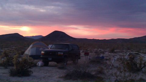 1986 Ford Bronco - Desert campsite scene with a Ford Bronco and tent under a vibrant sunset sky.
