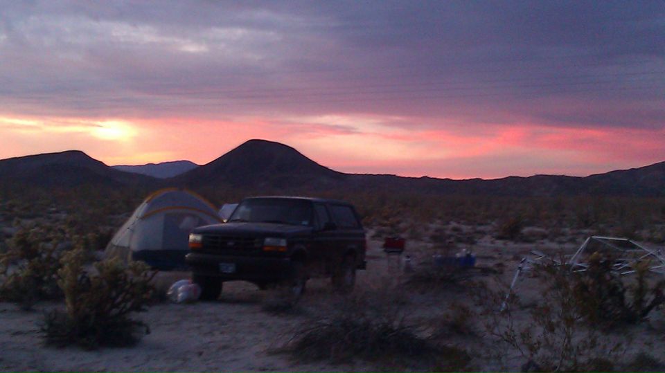 1987 Ford Bronco parked next to a tent in a desert campsite during a colorful sunset