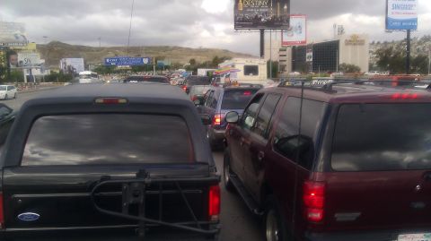 1986 Ford Bronco - A long line of vehicles are stuck in traffic on a cloudy day, with billboards visible in the background.