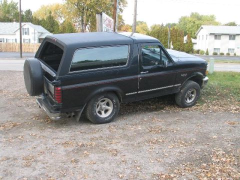 1993 Ford Bronco - This black 1993 Ford Bronco is viewed from the rear three-quarter angle, showing its spare tire mounted on the tailgate.