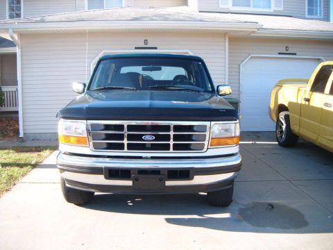 1996 Ford Bronco - This 1996 Ford Bronco is parked in front of a garage, with a yellow pickup truck visible to the right.