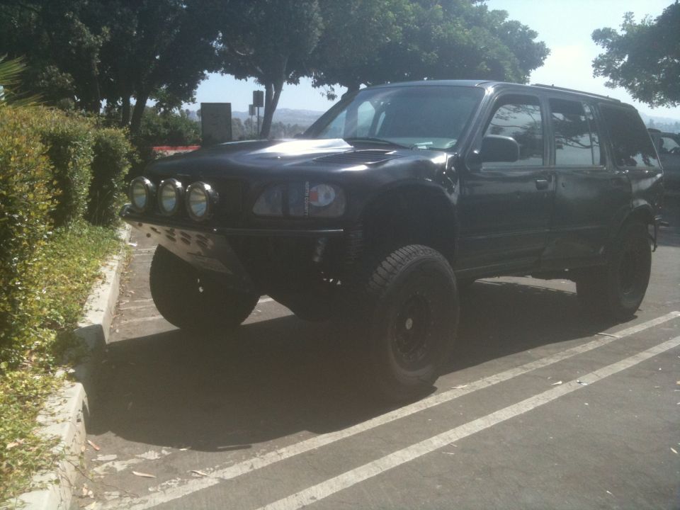 Black modified SUV with off-road tires, custom bumper, and auxiliary lights, viewed from a 3/4 front angle