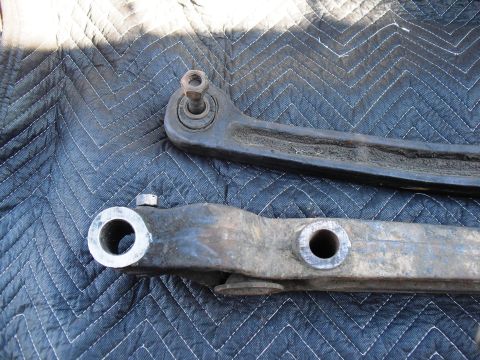 1986 Ford Bronco - Two used suspension control arms are laid out on a black quilted mat.