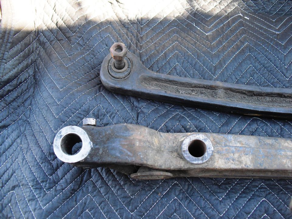 Two metal suspension control arms on a quilted mat. One arm has a ball joint end