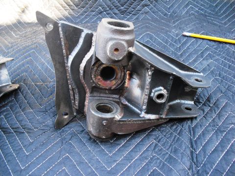 1986 Ford Bronco - A metal bracket assembly, likely a suspension component, is shown on a blue quilted surface. The part has visible welds and threaded fittin…