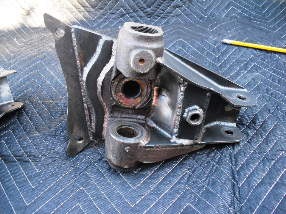 Metal bracket assembly with threaded fittings and bolt holes, resting on a quilted blue mat. Welded seams are visible